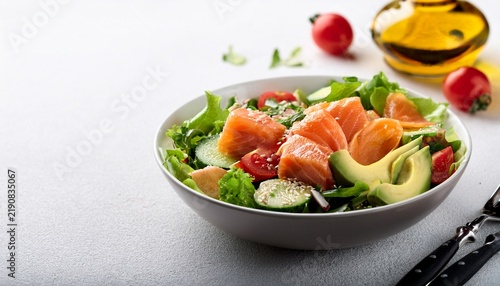 fresh salad bowl with avocado salmon and vegetables on bright table