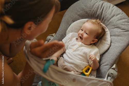 Obraz na płótnie Crying baby boy sitting in bouncer seat at home, upset toddler looking at mother