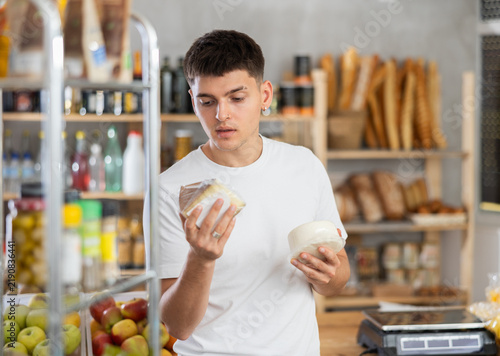 Thoughtful young male customer is deciding between kinds of cheese in a small market