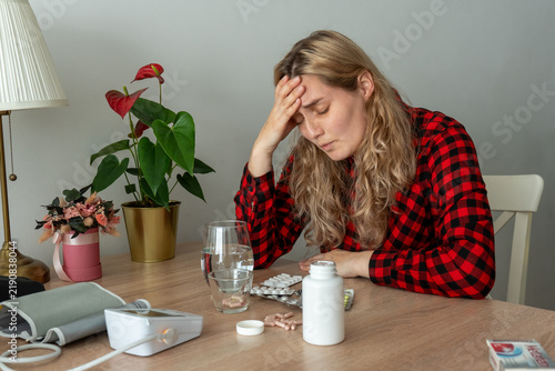 Overwhelmed woman sitting at table with medicine while holding her aching head. Concept of emotional burnout, chronic fatigue, depression, mental overload and difficulties of adult life.
