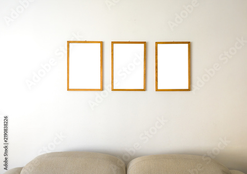 Three Empty Wooden Picture Frames Hanging Above Beige Sofa Couch on White Wall Mockup