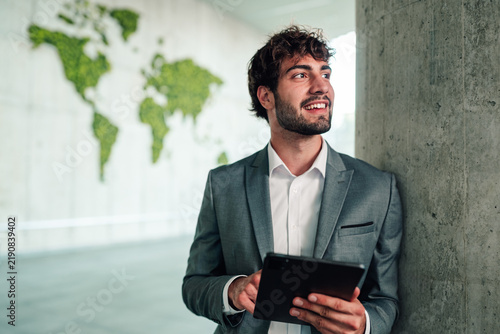 Quadro su tela Young businessman holding tablet, smiling, looking away, planning global busines