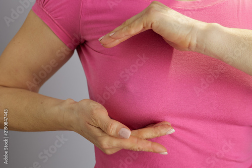 Close-up of a womans torso in a pink shirt framing her chest with her hands, illustrating breast health awareness and preventative medical education.