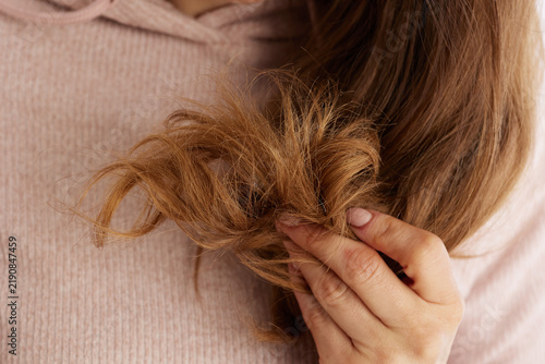 A detailed view of a woman holding a section of light brown hair, focusing on tangled and frizzy ends that need professional treatment and repair.