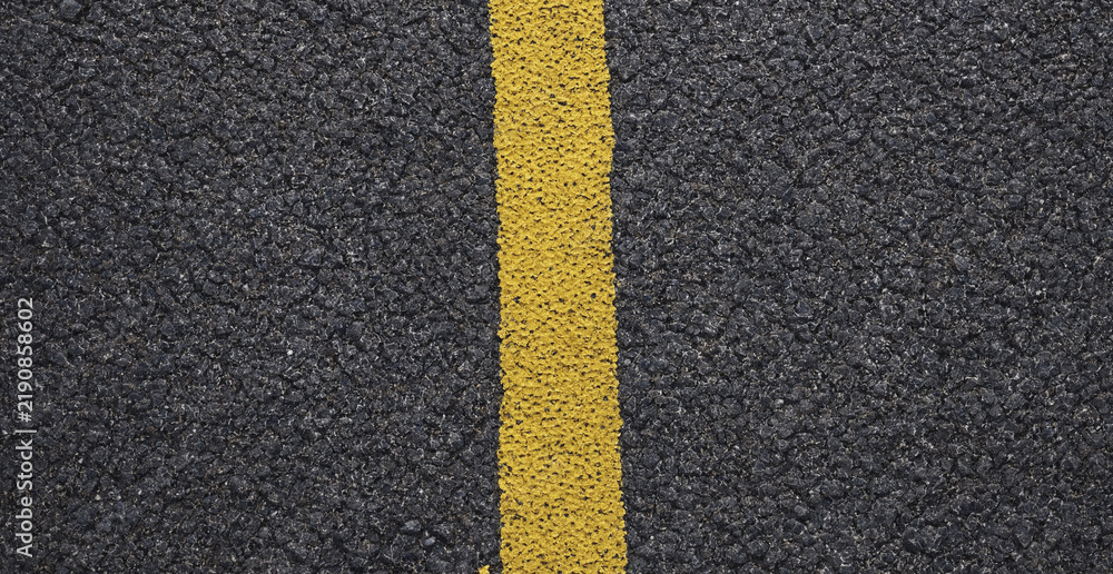 Obraz premium Top down view of a yellow painted line on dark grey asphalt road surface with textured pavement