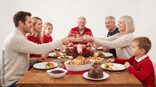 Multi generational family enjoying a festive Christmas dinner together around a wooden table laden with food