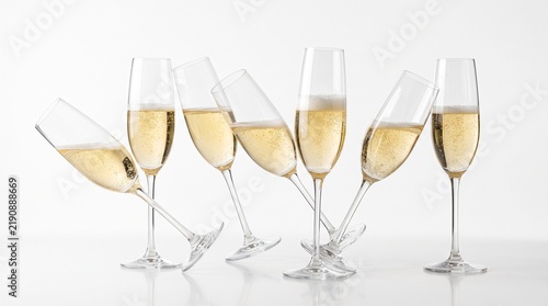Multiple champagne flutes filled with bubbly golden champagne and tilted in a playful arrangement