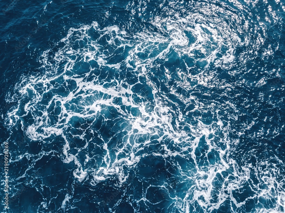 Fototapeta premium Turbulent ocean water with swirling white foam and dark blue depths.