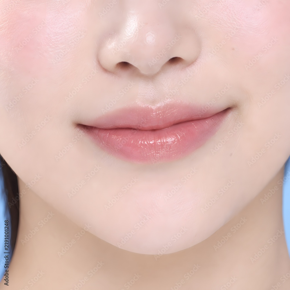 Obraz premium Close Up of Asian Woman with Soft Pink Lips and Smooth Skin on Light Blue Background