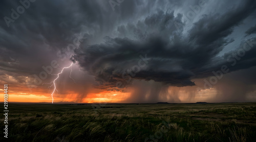 Dramatic lightning strike hitting the ground during a severe supercell thunderstorm over a rural landscape at sunset.