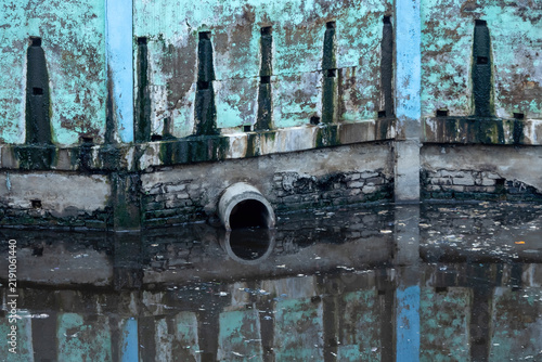 Cuadro en lienzo Industrial concrete drainage pipe protruding over stagnant dirty canal water with floating garbage debris