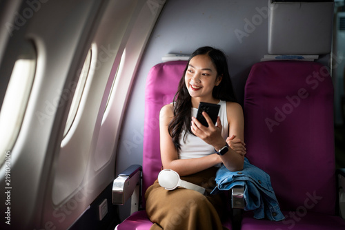 Woman Smiling and Using Phone While Sitting in Airplane Cabin Window View