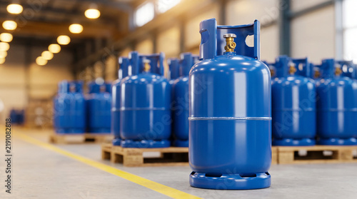 Rows of blue gas cylinders with brass valves stored on wooden pallets inside a large industrial warehouse