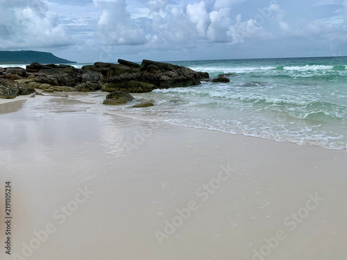 Foto Gentle waves washing ashore on a pristine white sand beach with rocks at Long Be