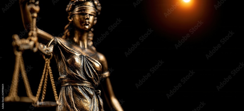 Fototapeta premium Blindfolded Lady Justice statue holding scales in dark background with light source