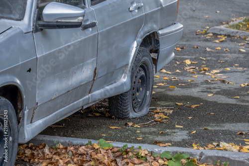 An old abandoned car is parked on the sidewalk on an autumn day