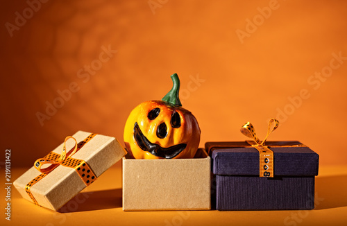 Jack o lantern emerging from gift box between wrapped presents on orange background for Halloween sale or party advertising