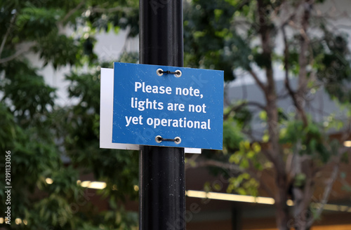 Konstfotografi A blue temporary notice sign attached to a black pole reading Please note, ligh