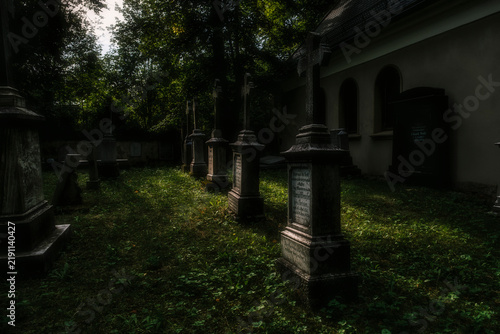 Quadro su tela A moody and atmospheric view of an old overgrown cemetery with weathered headstones and crosses surrounded by lush green foliage and dramatic lighting