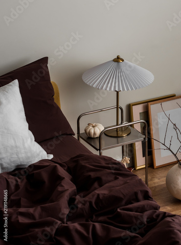 Cozy autumn interior of a bedroom - bed with brown bedding, autumn decor, lamp, ceramic vase. Cozy home concept