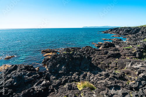 Black volcanic basalt reef and distant silhouette of Rebun Island, west coast of Rishiri Island