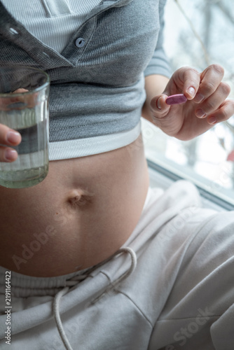 Asian pregnant woman is taking pills and vitamins for pregnant women with capsule on her hand and water. Drinking a tablet with a glass of water.