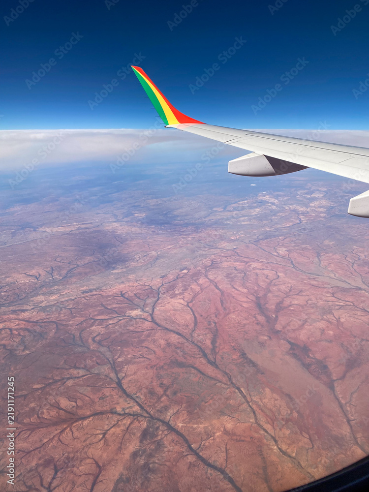 Fototapeta premium Airplane wing flying over arid desert landscape