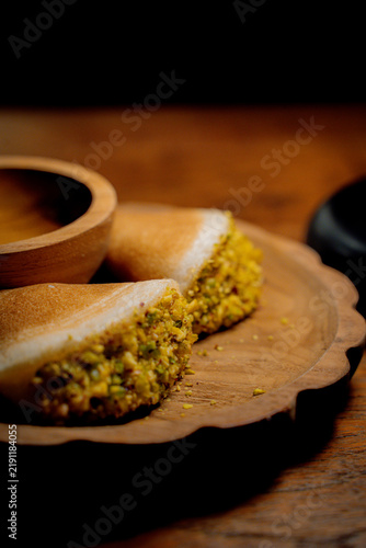 Traditional Arab qatayef pancakes folded around a pistachio filling and served with sweet syrup on a wooden plate.