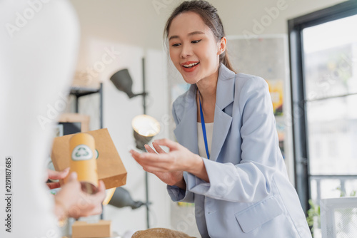 Принти на полотні Enthusiastic Asian businesswoman presenting recyclable packaging product to client during sales consultation, demonstrating persuasive communication, eco marketing, and sustainable entrepreneurship