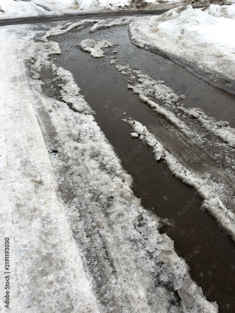 Obraz premium Snowy roadside with melting water flowing through icy channels