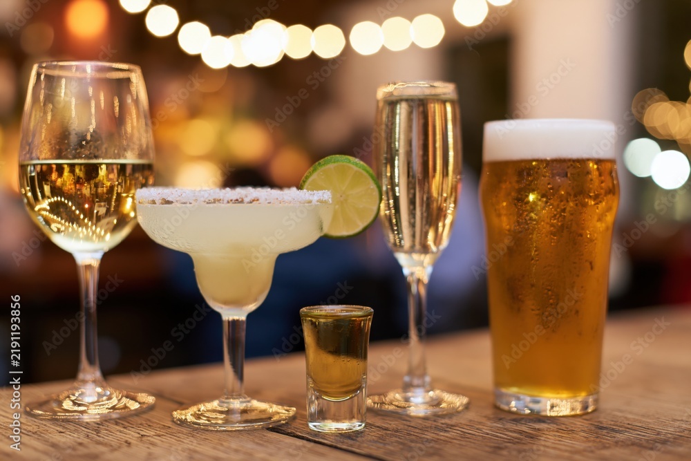Naklejka premium The Assorted Bar Drinks on Wooden Table Under Warm Bokeh Lights