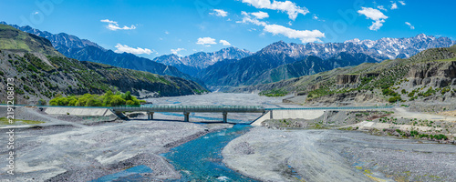 Принти на полотні Aerial view of a modern concrete bridge over a shallow rocky riverbed with mount