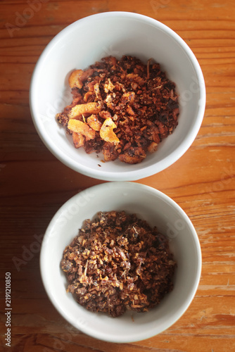 Pork crackling chili dip and ground fish chili dip in small white bowls on a wooden table.