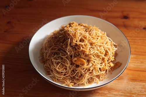 Stir-fried rice vermicelli with chili flakes, served on a white plate on a wooden table, ready to eat.