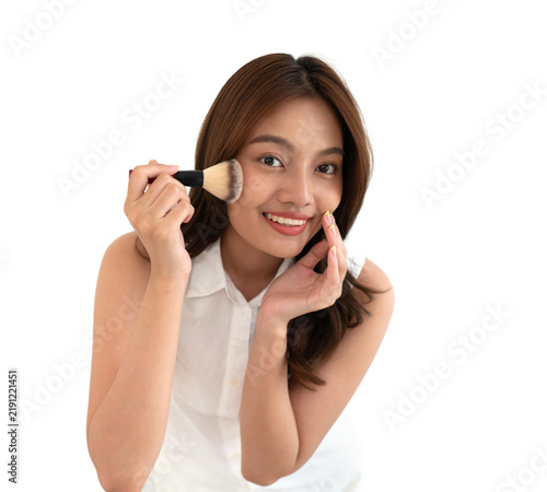 фотографія Young asian woman in a white sleeveless top is joyfully applying makeup using a brush