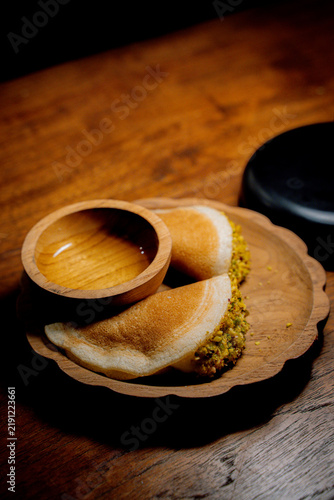 Traditional Arab qatayef pancakes folded around a pistachio filling and served with sweet syrup on a wooden plate.
