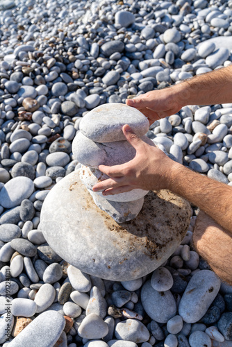 Photography Male hands building balanced stone stack pyramid on beach