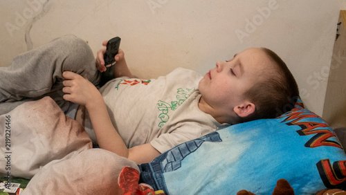 Фотография In a warm and inviting room filled with soft afternoon light, a child is comfortably nestled on a bed