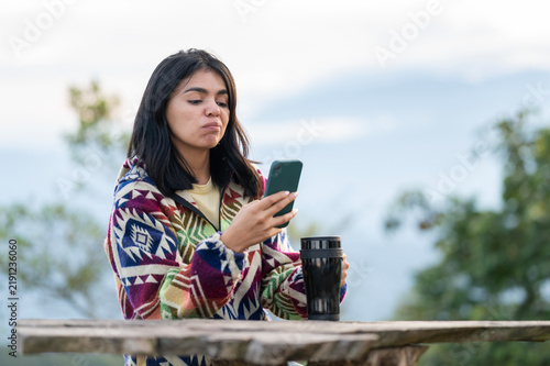 Woman using smartphone and drinking coffee outdoors in the mountains