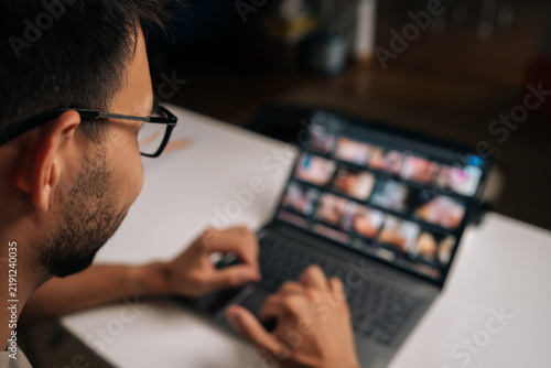 Foto View from shoulder of bearded man in glasses working on laptop at night, screen displaying adult content, potential misuse of technology or lapse in workplace ethics