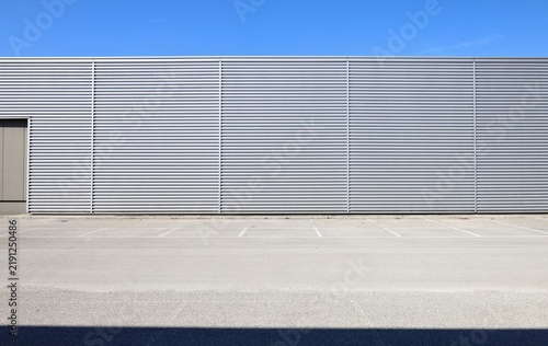 Corrugated metallic coating facade of a modern industrial building with empty parking lot in front. Blue sky above. Background for copy space