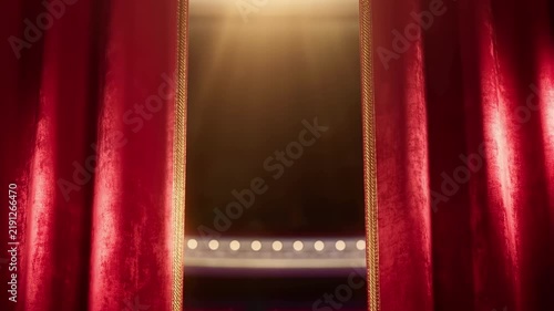 Grand opening of luxury red velvet theater curtains revealing a dimly lit stage with glowing footlights and warm atmospheric spotlights, ideal for cinema, drama, or performance art concepts.