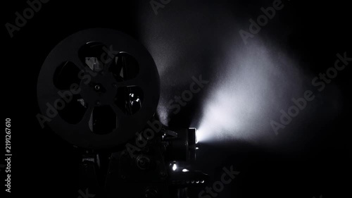 Vintage film projector operating in darkness with bright light beam and floating dust particles, creating a nostalgic cinematic atmosphere.