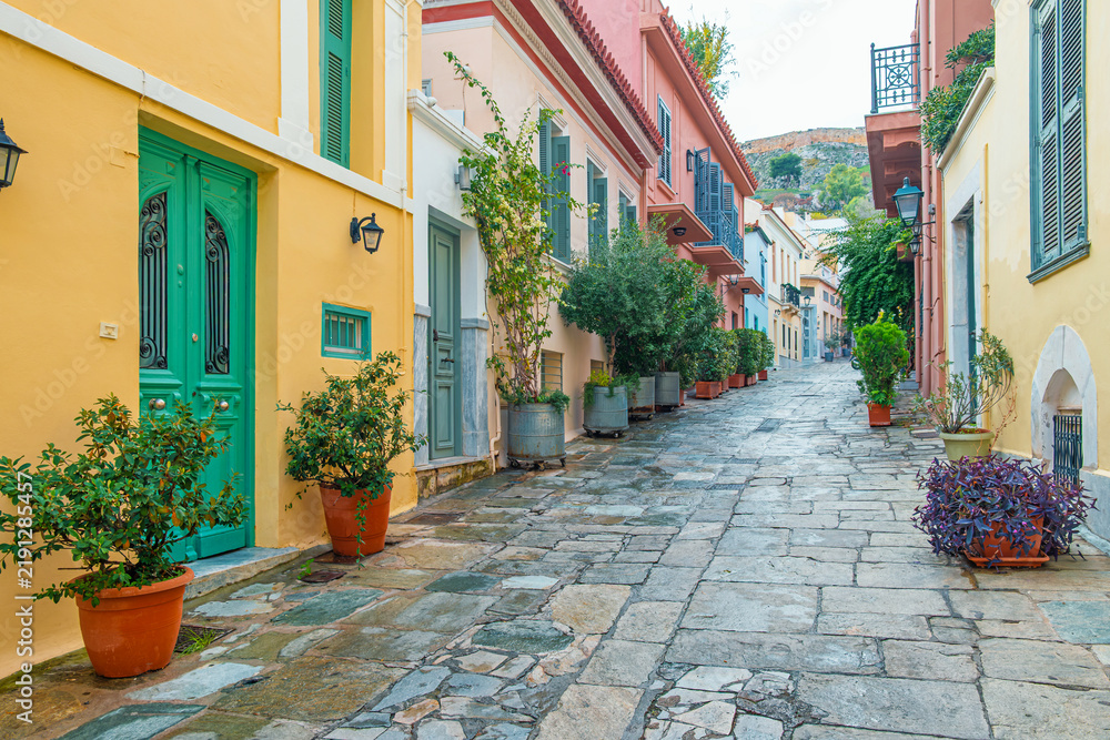 Obraz premium Stone paved street with colorful traditional houses, green doors and potted plants in Athens, Greece. Mediterranean architecture, European city travel, urban tourism and charming historic streetscape