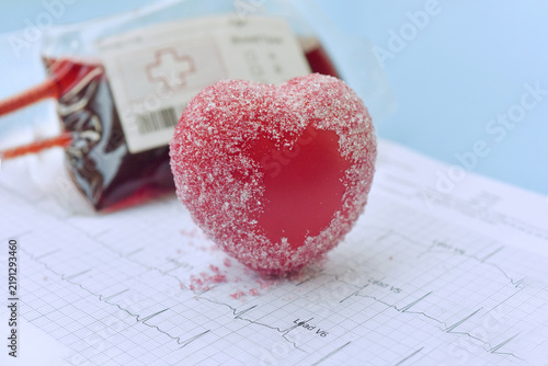 A red heart covered with sugar crystals with blood bag symbolizing the connection between diet, cardiovascular health, and blood sugar. 