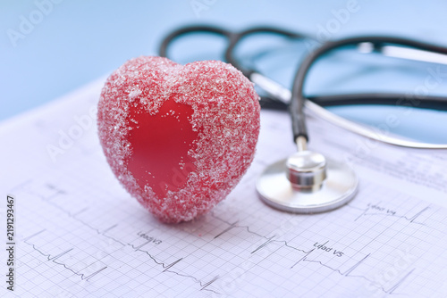 A red heart covered with sugar crystals is placed beside a stethoscope and an electrocardiogram (ECG,EKG) chart, symbolizing the connection between diet, cardiovascular health, and blood sugar