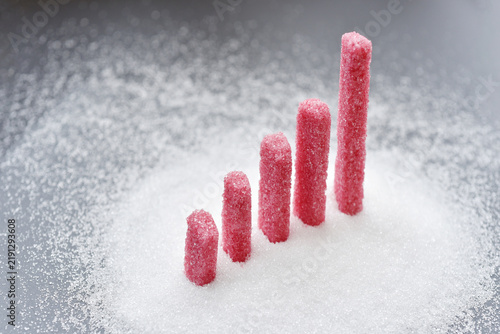 Sugar sticks arranged in ascending heights on a bed of white granulated sugar symbolize increasing sugar intake, rising consumption.