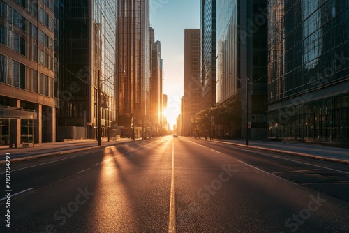 Empty asphalt road through a modern city framed by glass skyscrapers at golden hour