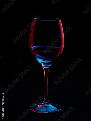 Close-up of a wine glass filled with red wine. the glass is standing upright on a black background. the wine glass is transparent and has a long stem with a round base.