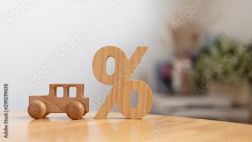 Auto loan interest rate and car finance discount concept with miniature wooden automobile beside percent symbol on table for vehicle leasing promotion, credit calculation and insurance cost.
